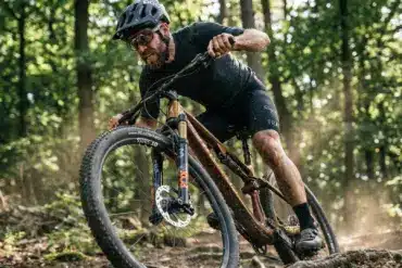 Ein Mann fährt ein goldfarbenes Storck Adrenalin Mountainbike auf einem Waldweg mit aufgewirbeltem Staub.