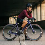 Frau mit Fahrrad, Storck Grix.3 Gravelbike, lila Rahmen, vor einer dunklen Betonwand stehend