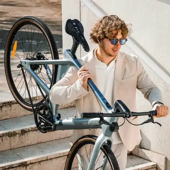 Ein Mann trägt ein leichtes Fiido Air E-Bike die Treppen hinauf. Das Fahrrad ist aus Carbon gefertigt und hat einen Riemenantrieb.