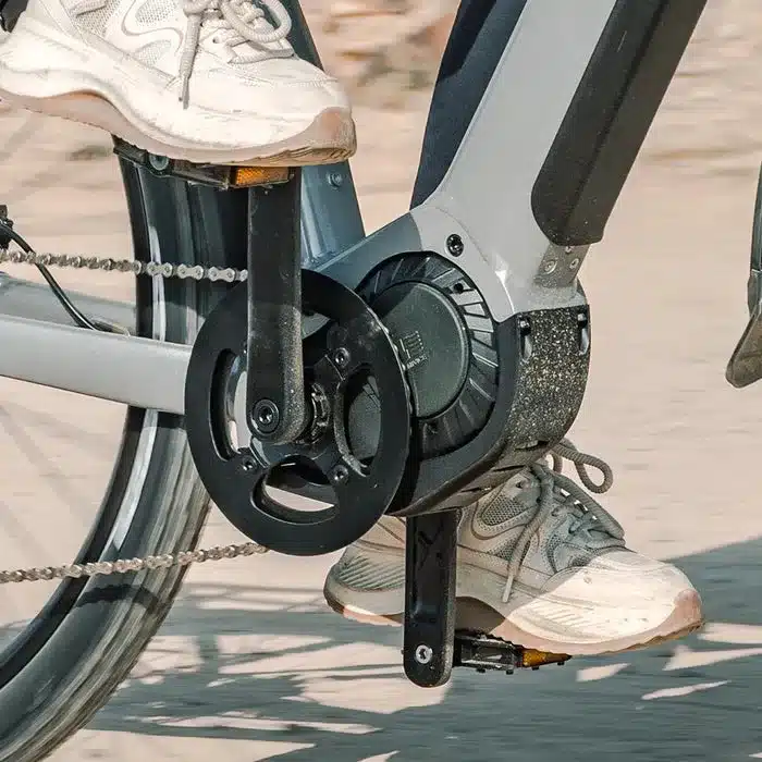 Nahaufnahme des Tretlagers und des Mittelmotors eines Fiido Nomads Pro E-Bikes, mit den Füßen zweier Personen auf den Pedalen.