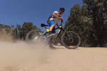 Ein Mann auf einem Haoqi Cheetah E-MTB mit schwarzem und gelbem Rahmen fährt auf einem staubigen Feldweg und wirbelt Staub auf.