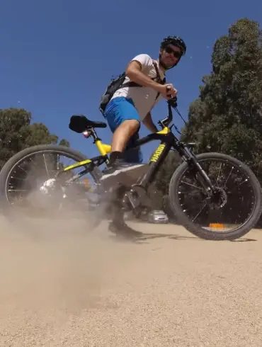 Ein Mann auf einem Haoqi Cheetah E-MTB mit schwarzem und gelbem Rahmen fährt auf einem staubigen Feldweg und wirbelt Staub auf.