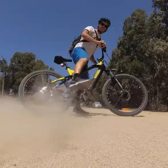 Ein Mann auf einem Haoqi Cheetah E-MTB mit schwarzem und gelbem Rahmen fährt auf einem staubigen Feldweg und wirbelt Staub auf.