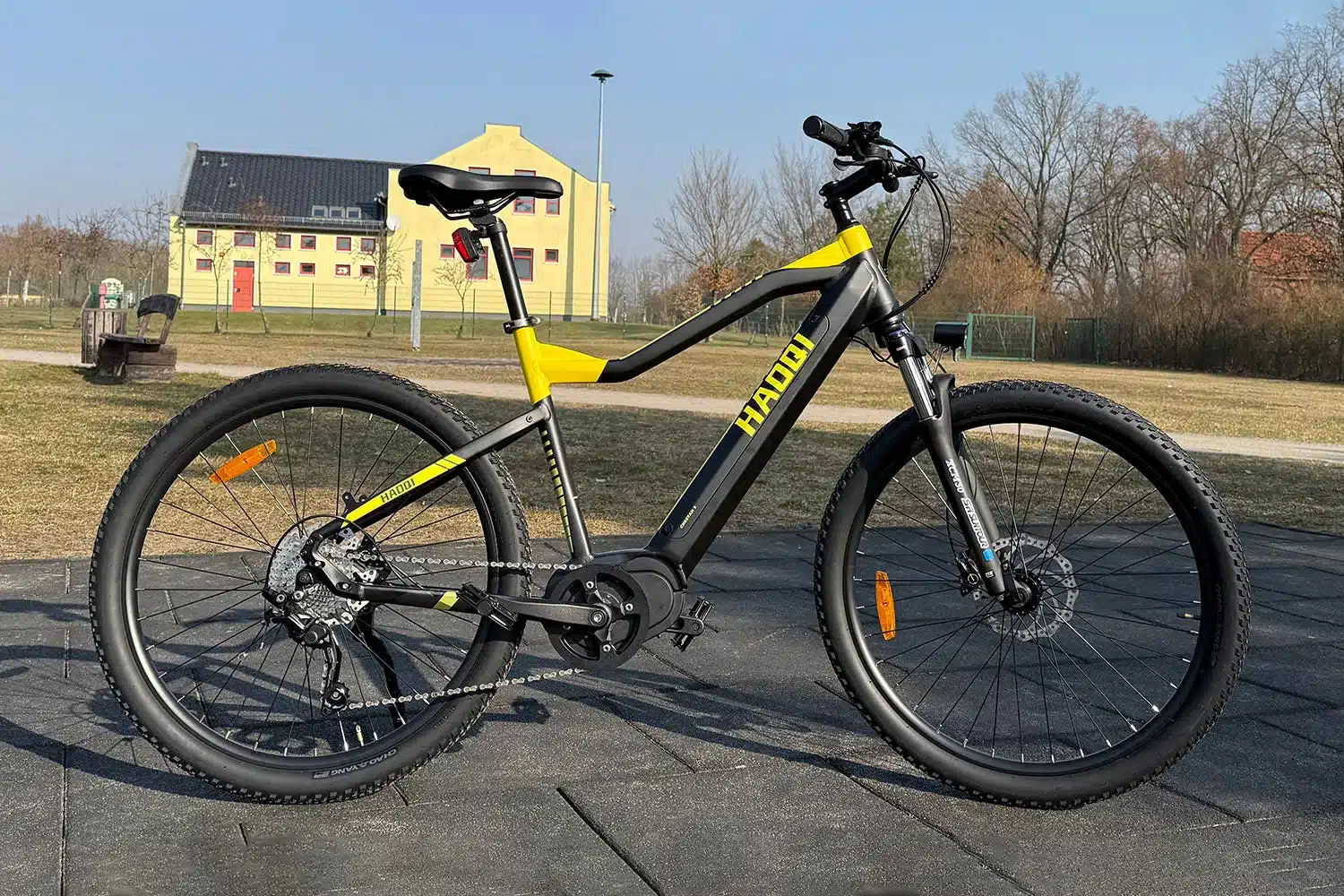Das HAOQI Cheetah All-Terrain E-MTB in Schwarz und Gelb steht auf einem gepflasterten Untergrund im Freien.
