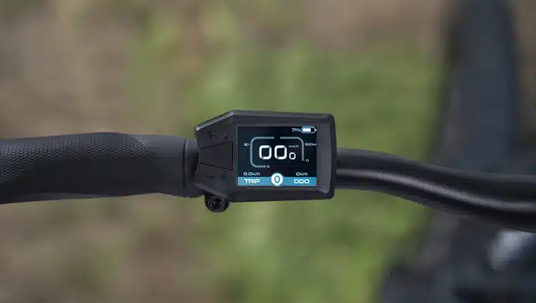 Nahaufnahme des farbigen LCD-Displays eines E-Mountainbikes, das Geschwindigkeit, Akkustand und Kilometerzahl anzeigt.