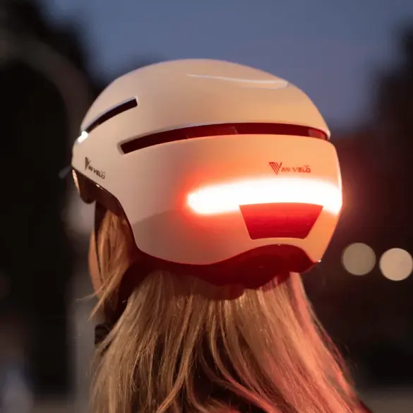 Fahrradhelm NOVA in Weiß mit aktiviertem rotem Rücklicht bei Dämmerung, gesehen von hinten auf dem Kopf einer Person mit blonden Haaren.