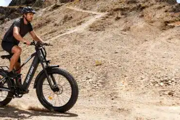 Mann fährt Rattan Pathfinder Pro E-Fatbike auf einem felsigen Bergpfad, Staub aufwirbelnd.