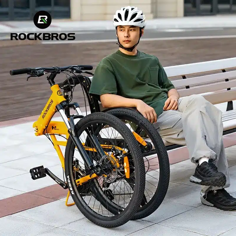 Mann mit weißem Helm und grünem T-Shirt sitzt auf einer Bank, daneben ein zusammengeklapptes gelbes ROCKBROS Fahrrad.