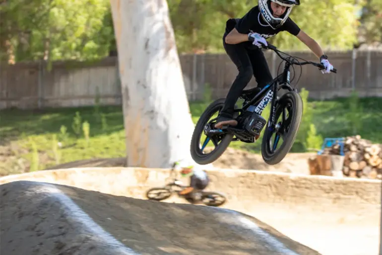 Ein Kind in voller Fahrt springt mit einem STACYC 20eDRIVE Elektrofahrrad über einen Dirt-Jump-Hügel.