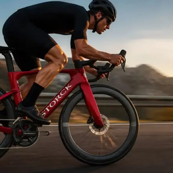 Rennradfahrer auf einem roten Storck Aerfast-Rennrad in aerodynamischer Position auf einer bergigen Straße bei Sonnenuntergang.