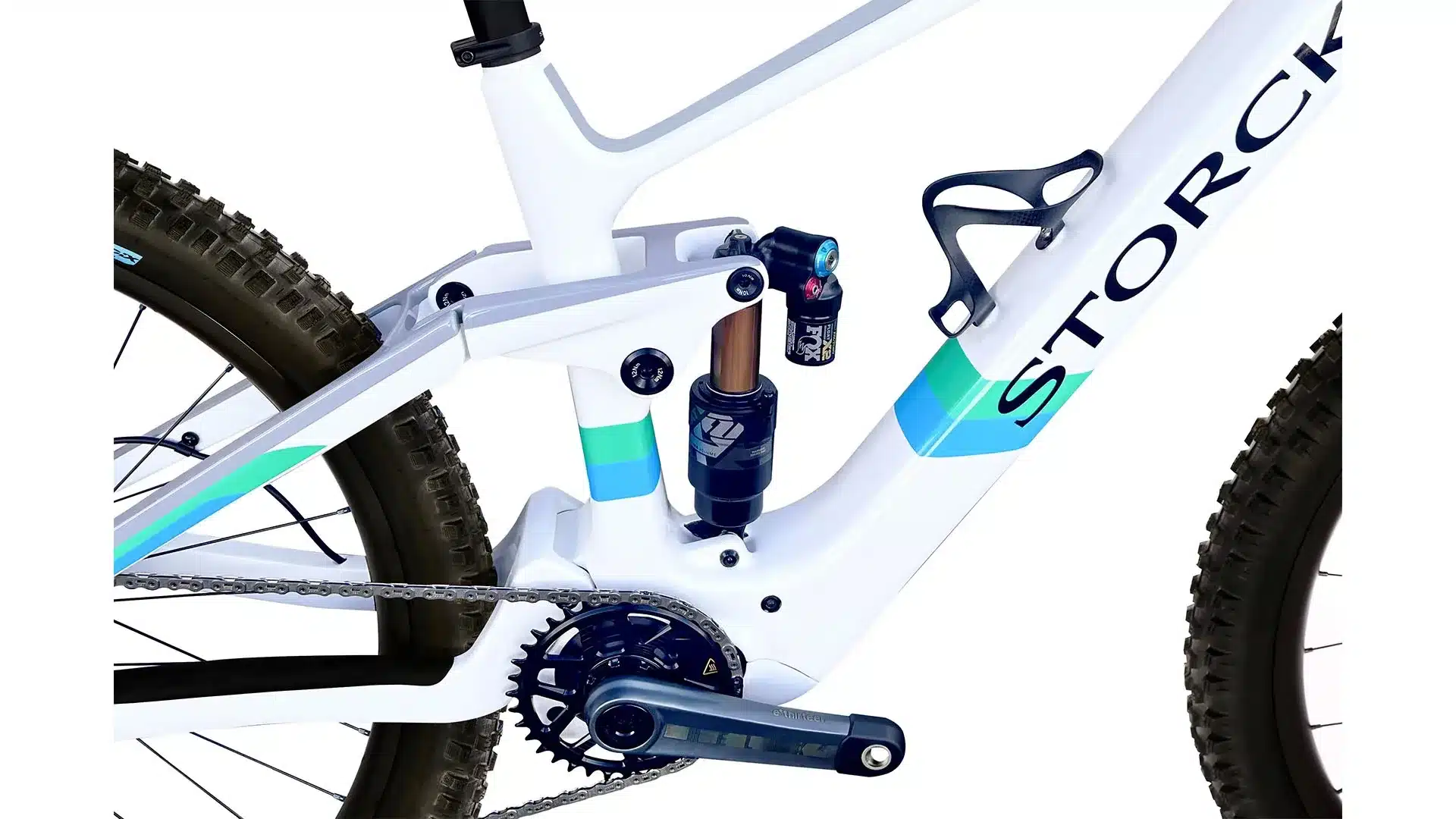 Detailansicht des Storck e:drenalin Carbon-E-MTB-Rahmens mit Fokus auf die Hinterradaufhängung, den Dämpfer und die Kurbelgarnitur. Das Fahrrad ist weiß mit grafischen Akzenten in Blau und Grün.