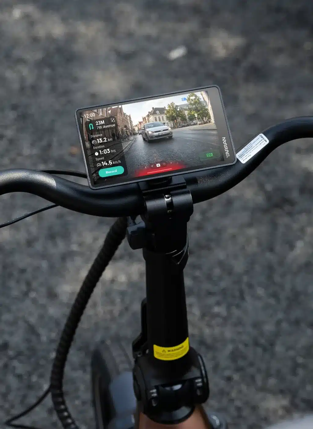 Digitaler Bildschirm eines TARRAN L1 Fahrrads zeigt eine Straßenansicht mit Gebäuden und einem fahrenden Auto, ergänzt durch Fahrdaten wie Distanz, Dauer und Geschwindigkeit.