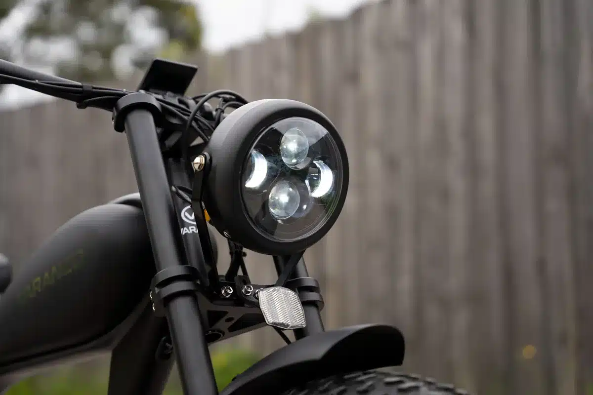 Frontpartie eines schwarzen Varaneo Café Racer E-Bikes mit rundem LED-Scheinwerfer, Lenker und Logo.