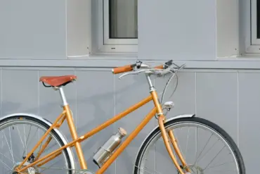 Seitenansicht eines orangefarbenen Capri Azur Stinger 4 E-Bikes, das vor einer grauen Wand steht.
