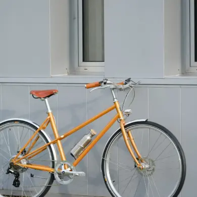 Seitenansicht eines orangefarbenen Capri Azur Stinger 4 E-Bikes, das vor einer grauen Wand steht.