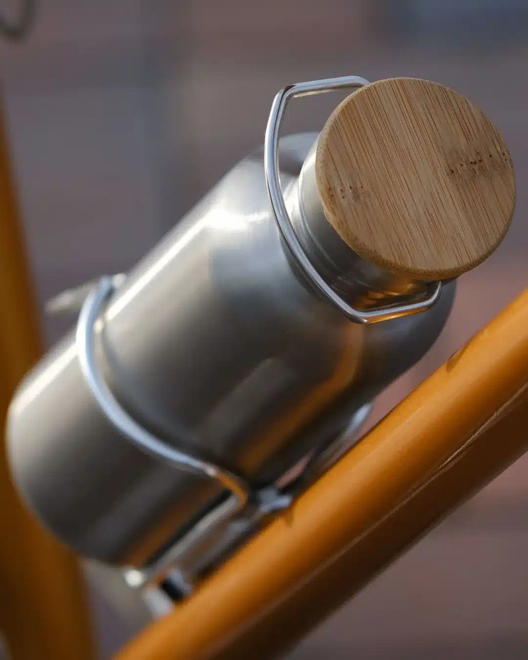 Edelstahl-Trinkflasche mit silbernem Halter und rundem Holzdeckel, befestigt an einem orangen Fahrradrahmen.