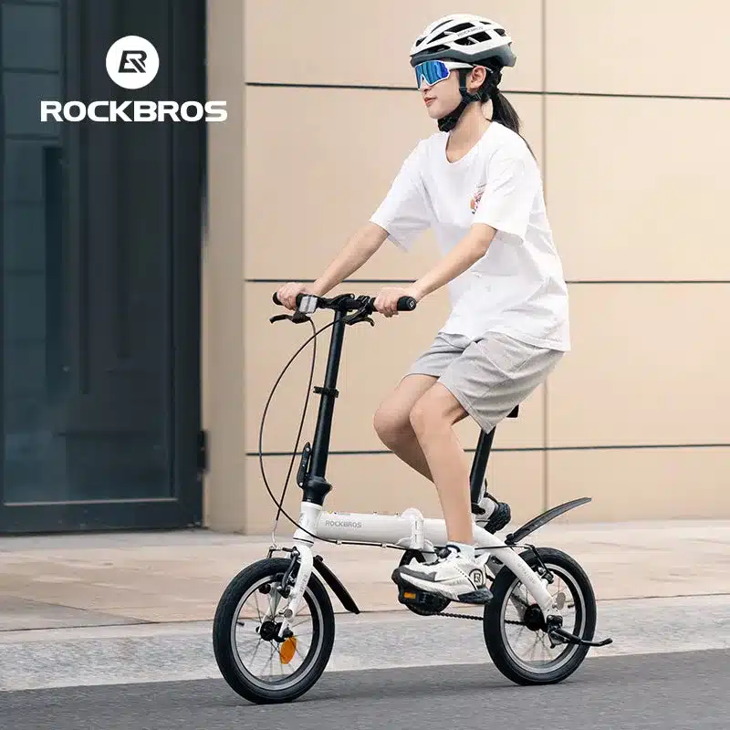 Eine Frau fährt ein weißes ROCKBROS IFN 14-Zoll-Faltrad in der Stadt, trägt Helm und Sonnenbrille.