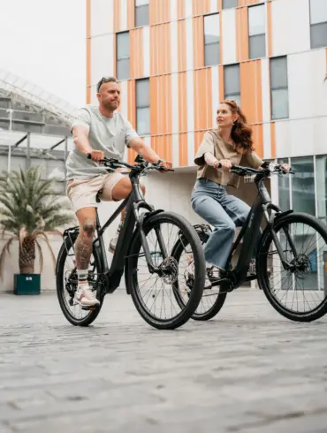 Mann und Frau fahren nebeneinander auf schwarzen AERES Leuven SX 9 Mid Step E-Bikes.