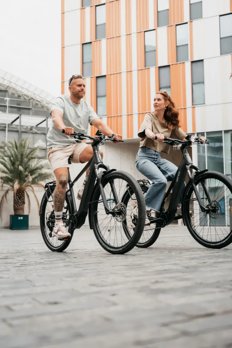 Mann und Frau fahren nebeneinander auf schwarzen AERES Leuven SX 9 Mid Step E-Bikes.