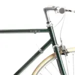 Detailansicht des YIWU+ Racing Green Citybikes, Fokus auf den grünen Stahlrahmen mit "YIWU" Schriftzug, den Lenker mit cremefarbenen Griffen und das cremefarbene Vorderrad mit silberner Felge.