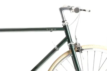 Detailansicht des YIWU+ Racing Green Citybikes, Fokus auf den grünen Stahlrahmen mit "YIWU" Schriftzug, den Lenker mit cremefarbenen Griffen und das cremefarbene Vorderrad mit silberner Felge.