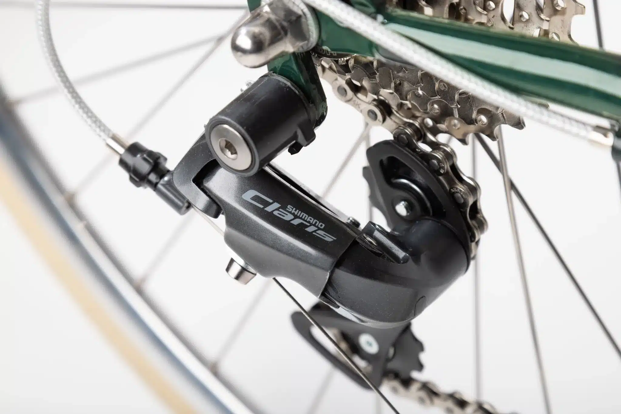 Detailaufnahme des schwarzen Shimano Claris Schaltwerks an einem grünen Fahrradrahmen, mit Blick auf die Kette und Kassette.