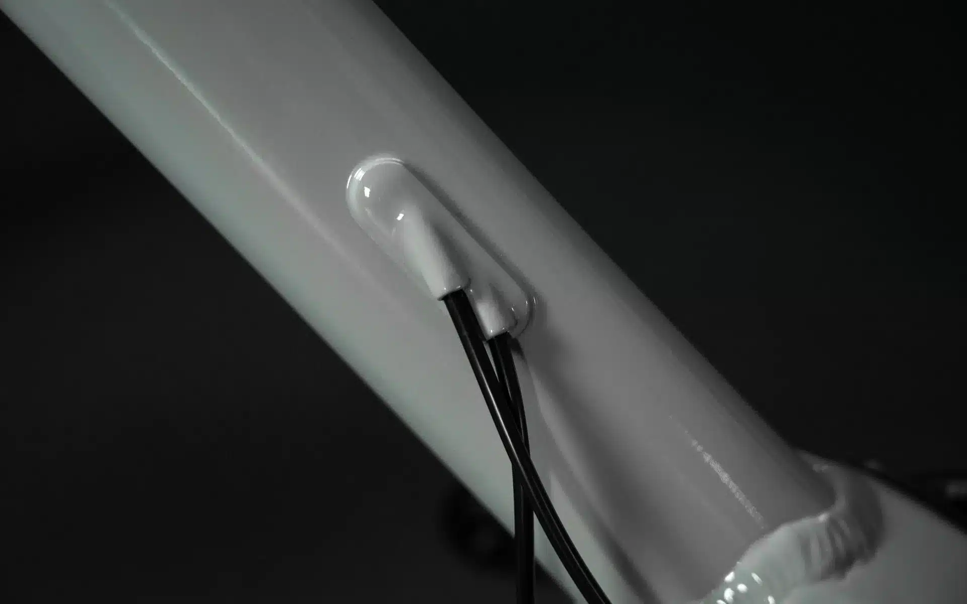 Nahaufnahme eines weißen Fahrradrahmens mit einer Aussparung, aus der schwarze Kabel für die interne Verlegung herausgeführt werden.