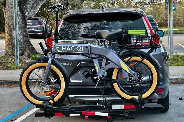 Graues faltbares Haoqi Squirrel E-Bike mit gelben Fat-Reifen, das auf einem Fahrradträger hinter einem dunklen SUV montiert ist.
