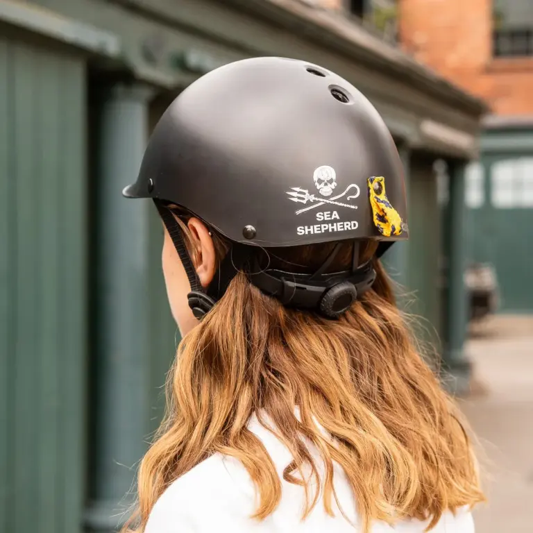 Eine Person trägt einen schwarzen City-Helm mit dem Sea Shepherd Jolly Roger Logo und einer bunten Schlaufe am Heck.