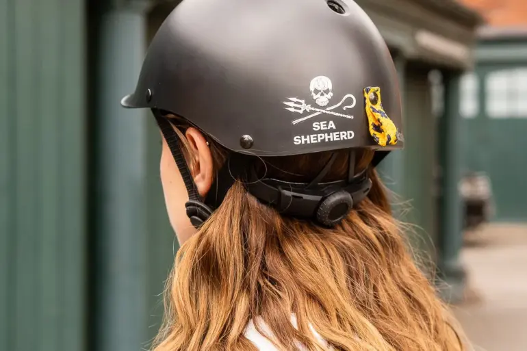 Eine Person trägt einen schwarzen City-Helm mit dem Sea Shepherd Jolly Roger Logo und einer bunten Schlaufe am Heck.