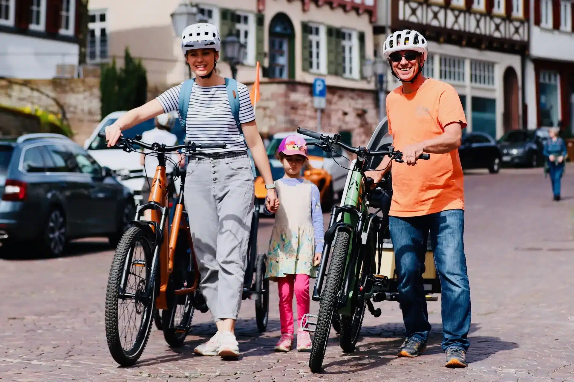 Ein Mann, eine Frau und ein Kind stehen nebeneinander mit E-Bikes in einer historischen Gasse.