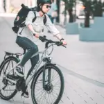 Frau fährt ein Husqvarna Towner B3 Urban-Bike mit Gepäcktasche auf dem Rücken, Helm und Sonnenbrille tragend.