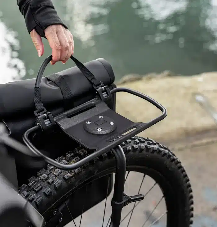 Nahaufnahme der Aeroe Urban Pannier Bag, die an einem Fahrradgepäckträger befestigt wird, mit Fokus auf das Befestigungssystem und das Rad.