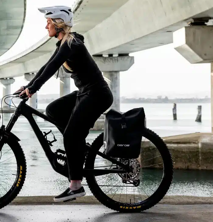 Eine Frau fährt ein Fahrrad mit einer schwarzen Aeroe Urban Pannier Bag, die am Gepäckträger befestigt ist.