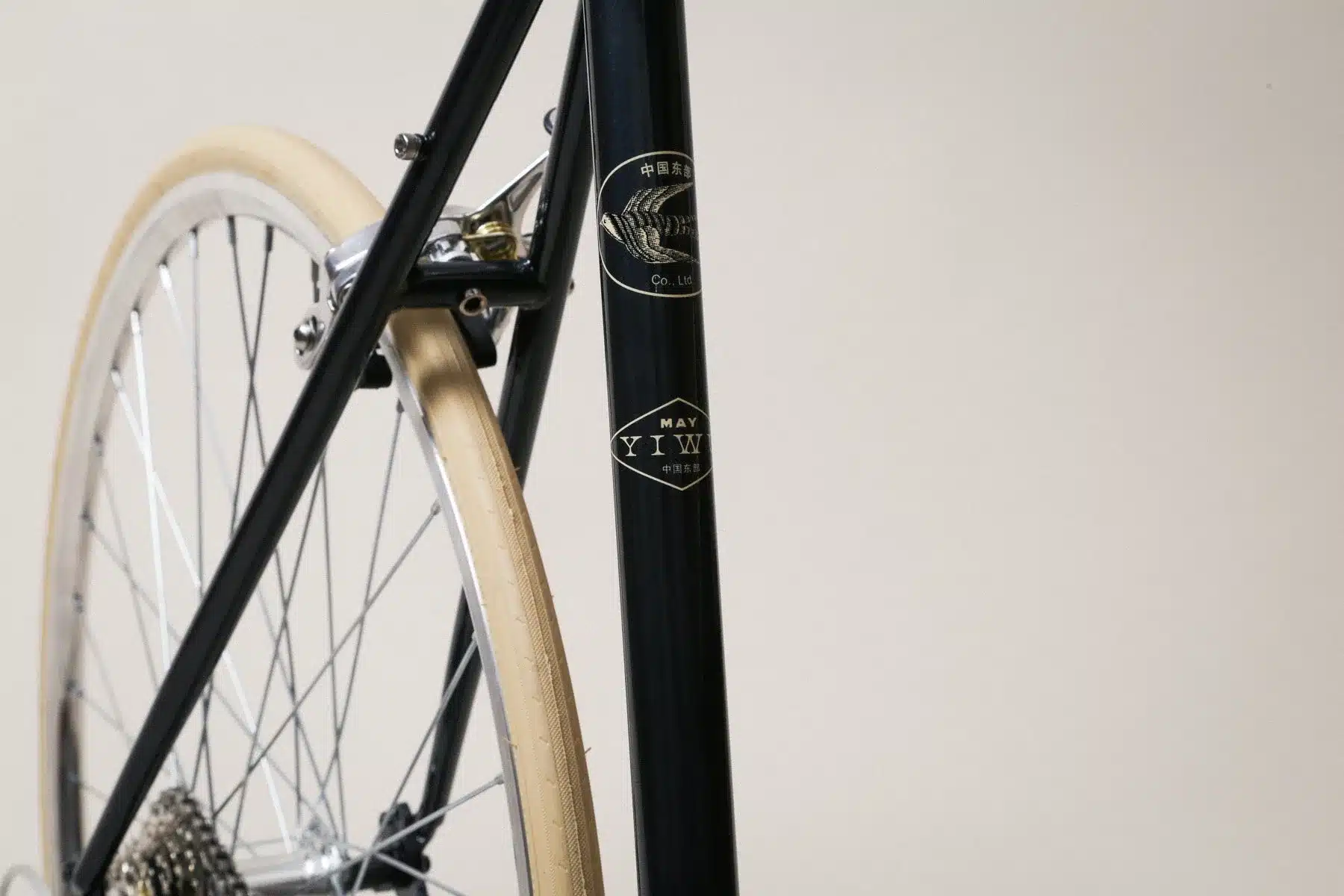Nahaufnahme des schwarzen Rahmens eines YIWU Citybikes mit silbernen Speichenrädern und cremefarbenen Reifen. Das YIWU-Logo ist deutlich sichtbar.