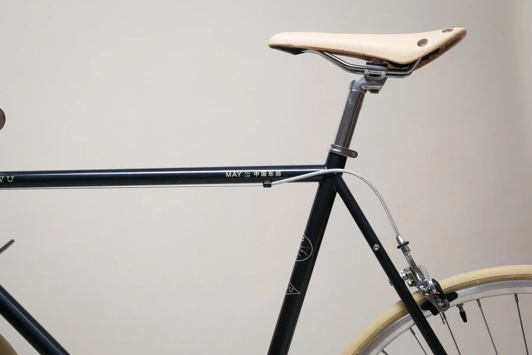 Nahaufnahme des YIWU Night Blue Citybikes, Fokus auf den oberen Teil des Rahmens mit dem Schriftzug 'MAY Co., Ltd 中国东部', dem silbernen Sattelgestell und dem hellbraunen Ledersattel.