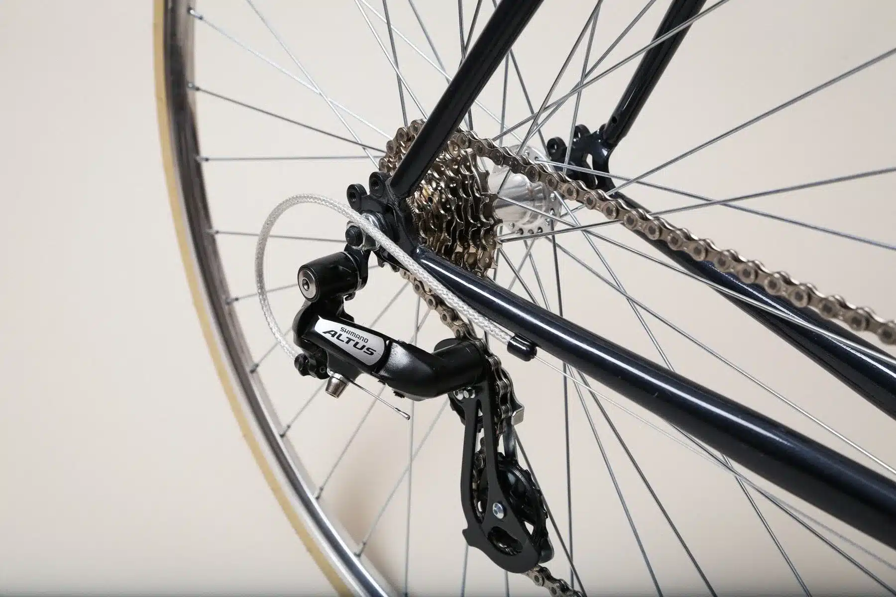 Nahaufnahme des Hinterrads eines schwarzen Citybikes mit silberner Kette und goldfarbener Kassette. Das Schaltwerk von Shimano Altus ist sichtbar.